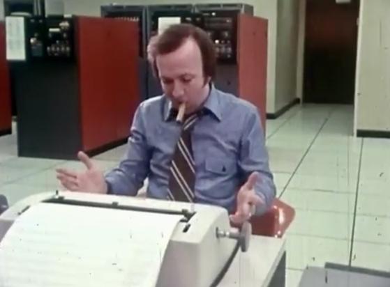 Man at a teletype in a computer centre chomping a cigar.