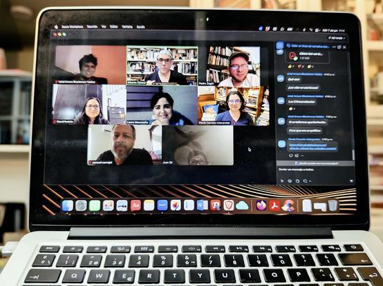 Una laptop muestra la pantalla de una videollamada con un grupo de ocho personas, que sonríen a la cámara.