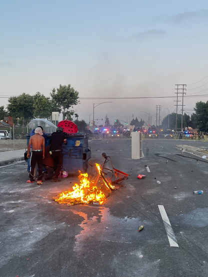 Protestors barricaded behind a dumpster, facing off against a line of law enforcement vehicles.