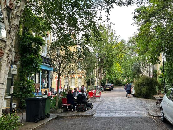 Cafe on a street in Lambeth, London. Notable because it is nice and green, people are sat outside a cafe eating. It feels safe, intimate, inviting and human scale.