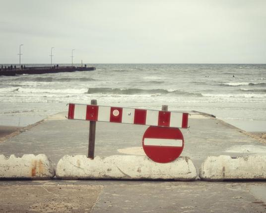 Betonweg der im Meer endet, abgesperrt mit einem Einbahnstraßenschild.