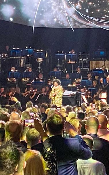 Dame Shirley Bassey on stage in a gold-coloured sparkling dress.