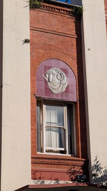 A merino ram's head against square maroon tiles framed by an arch of red bricks.