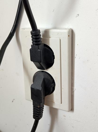 A double Schuko plug socket with two right angled Schuko plugs plugged in: one with the cable coming out on the bottom, one with the cable awkwardly coming out the top.