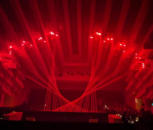 A darkened theatre roof with multiple red lasers lighting it up, forming a parabolic shape.