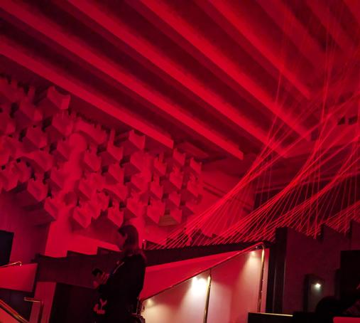 A darkened theatre with multiple red lasers appearing to form helix shapes.