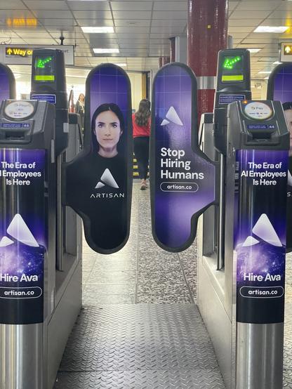 An advertisement featuring a woman’s portrait is placed on automated turnstiles in a transit area. The text reads "Stop Hiring Humans" and "The Era of AI Employees Is Here," promoting a service related to AI solutions.