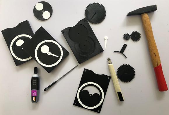 Workbench during the assembly of lunar moon phase calculators, showing parts, glue, tools, and two complete mechanisms.
