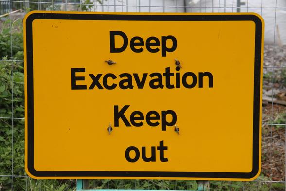 Photograph of a large, rectangular yellow sign clipped to a wire fence. There are four lines of black text on it, with one word per line, reading "Deep Excavation Keep out" 

And yes, the lack of a capital letter on the last line is bugging me as much as it is you.
