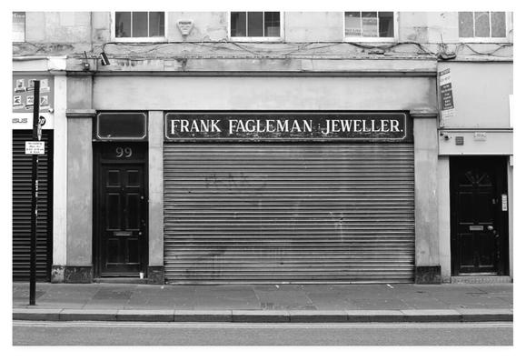 Black and white photograph of a closed jewellery shop with the metal shutter pulled down.