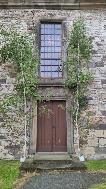 Eingang der Trinitatiskirche Gleina mit Pfingstmaien auf beiden Seiten der Eingangstür