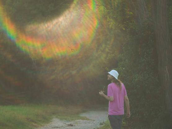 A coulour photo of a man looking to the right. In this direction there is a rainbowshaped sunflair