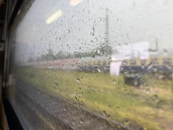 Picture of a window and some train carriages vaguely visible. Lot of rain droplets on the window.