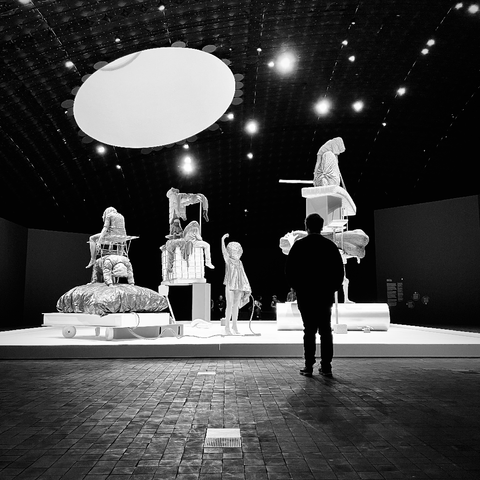 A visitor gazes at an art installation featuring surreal sculptures in a dimly lit space in Amos Rex museum.