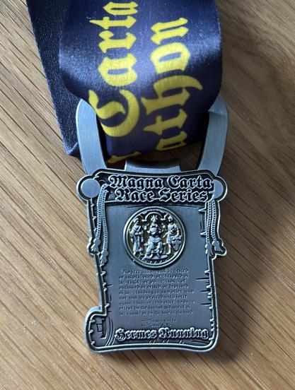 Medal which is also a bottle opener with Magna Carta race series on it. The medal looks like a scroll on a black ribbon.
