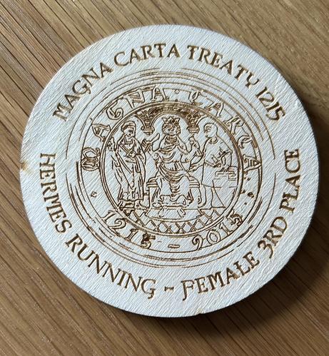A wooden engraved placemat with Magna Carta stamp on it and female 3rd place in the text.