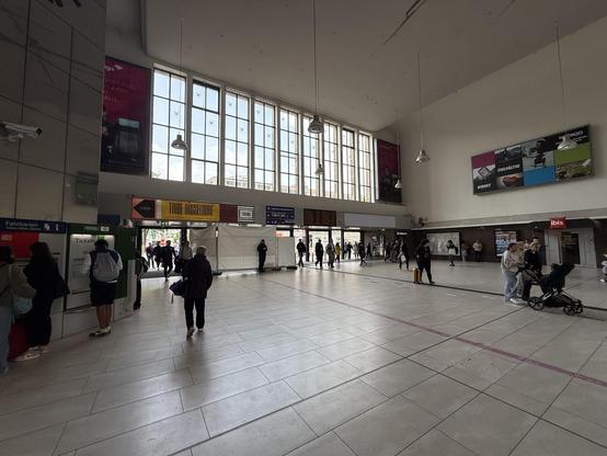 Inside a large hallway cq entrance of the Düsseldorf Hbf station. Some people left and right. Big windows up ahead.