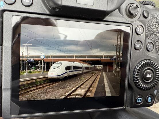 Photo of a photo camera screen showing a train at a platform. White high speed train with a blue band at the bottom.
