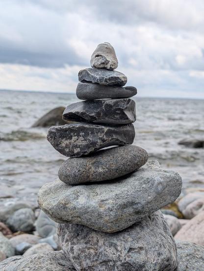 Gestapelte Steine am Strand mit dem Meer im Hintergrund.