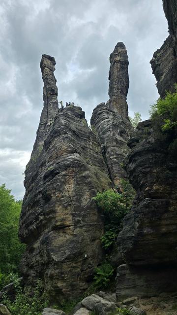 Mehrere hohe, schlanke Felsnadeln ragen in den bewölkten Himmel. Auf einer der Nadeln sind oben mehrere Kletterer zu erkennen.