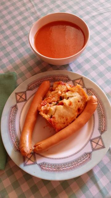 Un cuenco con gazpacho y un plato plano con dos salchichas y pastel de calabacín.
