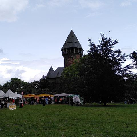 In der Bildmitte ein mächtiger Burgturm, der Bergfried der Burg Linn. Auf der Wiese davor einige bunte Marktstände. Erstaunlich wenige Menschen.