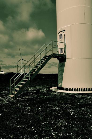 Part of a staircase from a wind turbine in the foreground. Two more wind turbines can be seen in the background. Taken on the Danish coast.