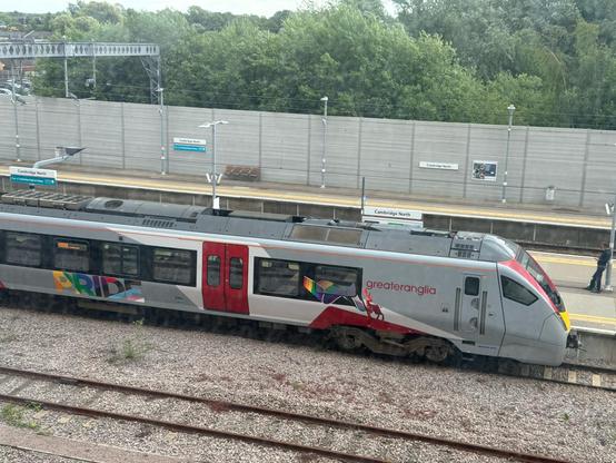 A Stadler FLIRT train. A regional Greater Anglia train in grey, with crimson door highlights and a progress PRIDE sign on the side.