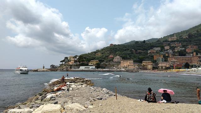 A surfer riding a nice, small wave at the bay of Recco; two more surfers approaching.