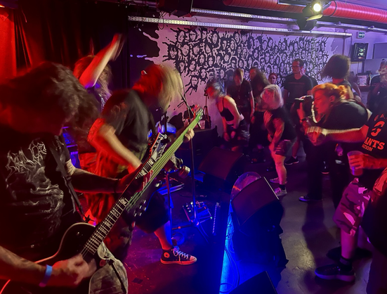 Bild von seitlich der Bühne mit rechts den Musikern und links dem headbangendem Publikum