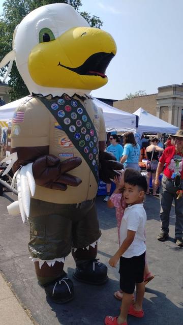 Baldy the Eagle Scout, a giant inflatable eagle costume who is wearing a Class A uniform, standing to the side of two young kids.