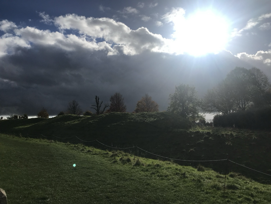 Long shot if the raised banks at Avebury with dramatic light from behind cloud.