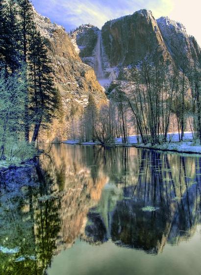 Winter Falls

This is an image of Yosemite Falls captured from the Swinging Bridge during a cold winter morning.
The Merced River flows in the foreground. There are small pieces of ice floating down the river but more importantly is the reflection of Yosemite Falls in the still water of the river.
The left bank of the river is composed mostly of tall pine trees. The right bank has mostly hardwoods growing along the river.
Yosemite Falls towers over Yosemite Valley. There is ice on both sides of the waterfall as it was cold enough for the mist to freeze against the rocks during the night.
