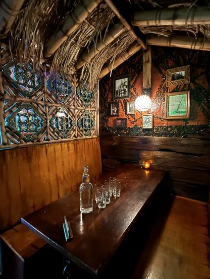 A booth at Inside Passage. Jade Tiles in bamboo sit above the back of the bench on each side and separates the booths
there are glasses and a large glass bottle.of water waiting.