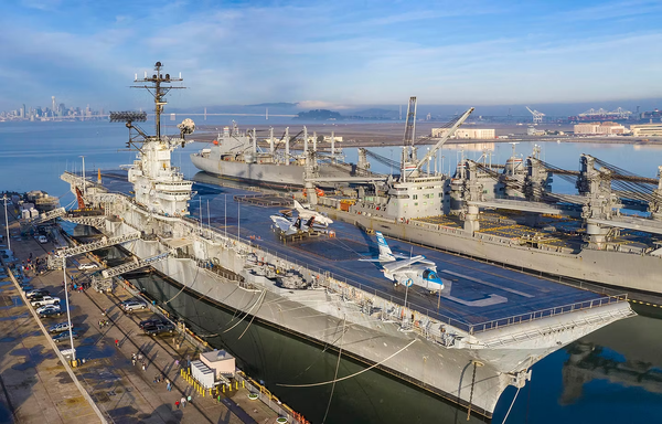 The USS Hornet sits at pierside at the Oakland museum. A few museum aircraft aboard and other ships nearby.