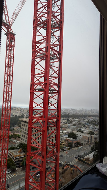 View northwest from upper floors of SF building with two red construction cranes and a foggy SF city in background
