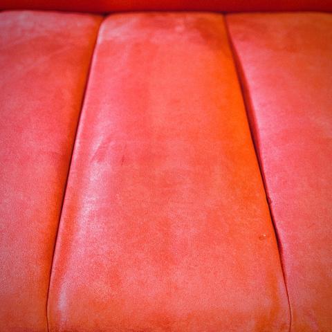 A view down from above a bright red couch shows its soft, ribbed back up to its seat, all reflecting muted sunlight from out of frame left.