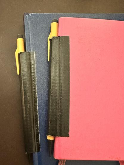 Two hardback notebooks (one blue, one pink) with yellow mechanical pencils duct taped to the spine