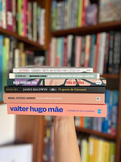 A hand holding 6 books in front of a book shelf