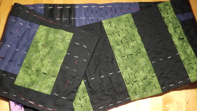 Photo of a patchwork scarf in green, purple, blue, & black with lines of kantha running stitch covering about 2/3 of it.