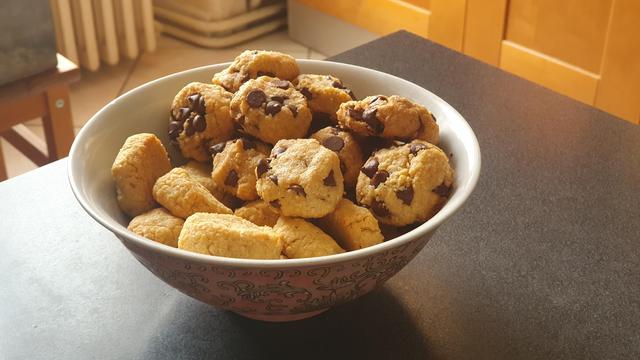 A bunch of small but very round cookies in a bowl. Only half of them have chocolate chips.