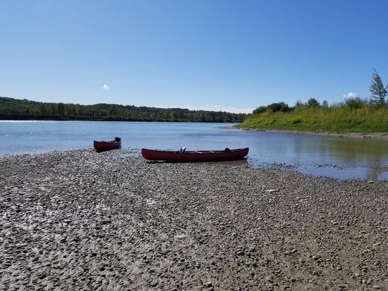 two red canoes on a ~sandy bar in the middle of a wide river