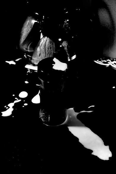 A very high contrast black and white, vertical image of the part of a kitchen bench with the coffee pot in the background, a spice jar with black pepper in the middle. 
Some light liquid has been splattered on the coffee pot, the lid of the spice jar, and the bench. The shape of the spilled liquid in front of the jar looks like a penis. Sorry about that, but true.