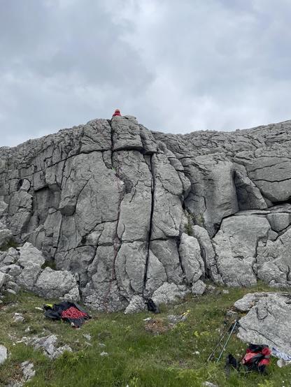 A limestone rockwall with the lead climber on top and a red rope along the prtection marking the new route Broken Button. Some gear at the bottom of the rock.