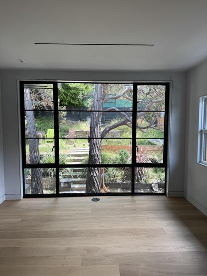 a photo of our bedroom post renovation, with large (fake) steel windows overlooking an incredibly overgrown backyard