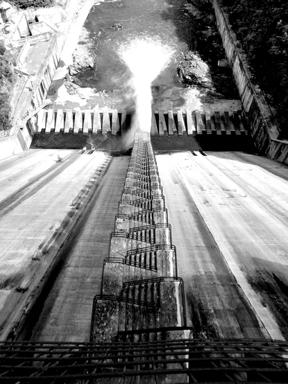 View of a dam from above. Some stairs go down to a place where a strong shoot of water flows to a river