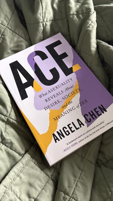 A close-up photo of the book Ace: What Asexuality Reveals About Desire, Society, and the Meaning of Sex by Angela Chen, resting on a quilted green blanket. The book cover features bold black and purple text with abstract yellow and lavender shapes.