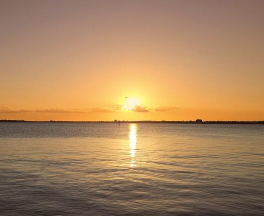 Golden sunset over a vast blue river as a helicopter flies in front of the sun.