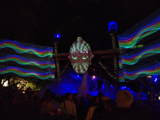 Die Deko der E-Stage auf dem Wilwarin Festival. Ein mit Laser beleuchtetes Gesicht, links und rechts davon farbige Lichtreihen.