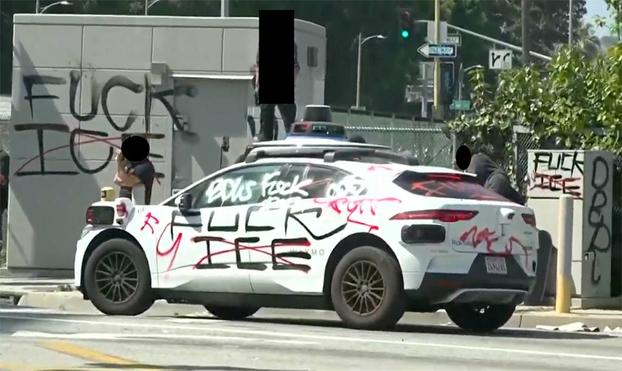 screenshot from livestream of the Los Angeles popular defense actions against the regime. A Waymo vehicle has been beautified with numerous spraypainted slogans saying things like "FUCK ICE"